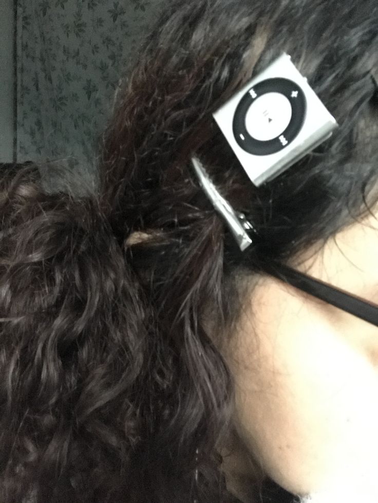 Close-up of curly-haired person using a silver iPod Shuffle as a hair accessory.