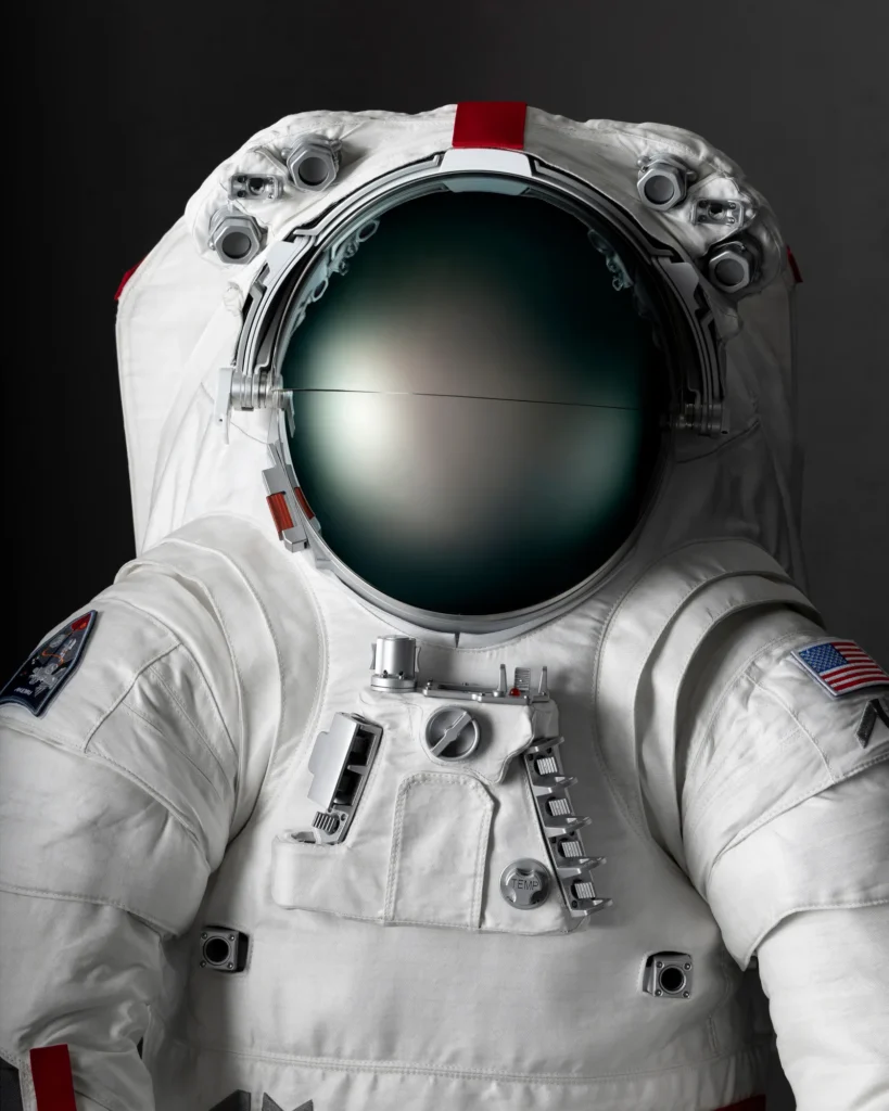 Close-up of the Helmet and Chest of the Prada Spacesuit: The helmet is large, round, and reflective with a dark visor. The chest panel has various compartments and controls, with both the American flag and Axiom Space logos visible on the suit's upper arms.