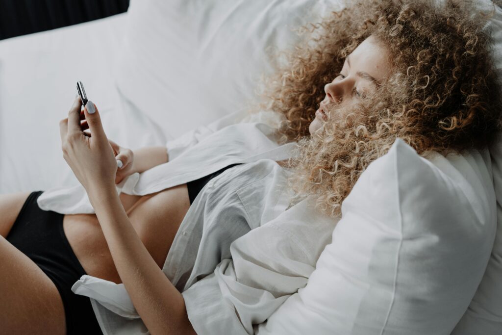 blonde girl with curly hair texting in bed