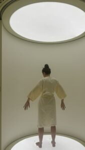 A patient stands under a circular light in a glowing chamber wearing a robe, capturing Neko Health’s unique futuristic health-scanning environment.