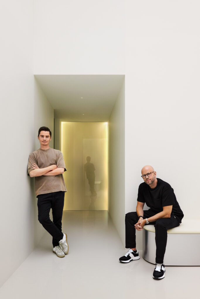 Two men, co-founders Hjalmar Nilsonne and Daniel Ek, pose in a sleek hallway with a glowing light, showcasing Neko Health’s modern and minimalist design ethos.