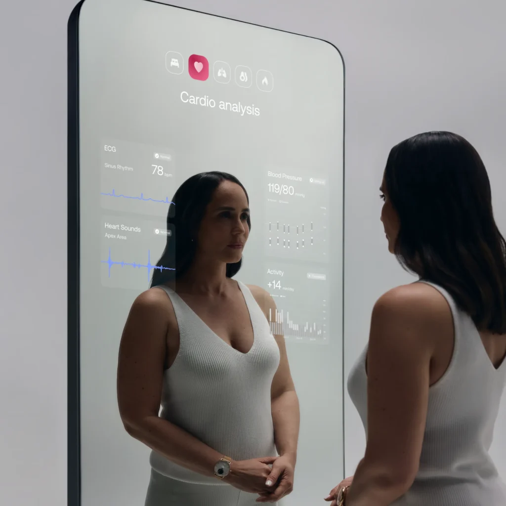 The Withings Omnia is a futuristic smart mirror that doubles as a health tracker. A woman stands before the sleek, full-length mirror, which displays her vital health metrics like heart rate, blood pressure, and activity levels. The design is minimalistic, blending seamlessly into a modern health-conscious lifestyle.