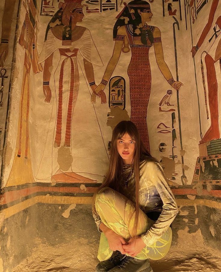 This may contain: a woman sitting on the ground in front of egyptian paintings