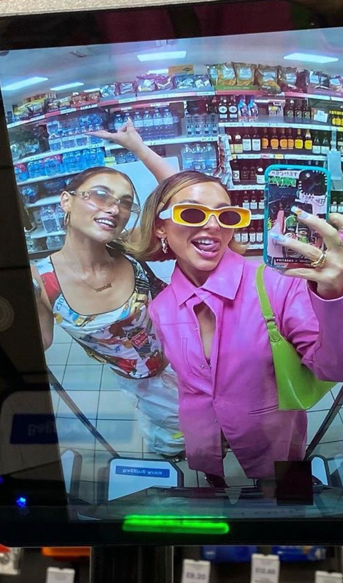 This may contain: two women in pink are on the television screen and one is holding up her cell phone