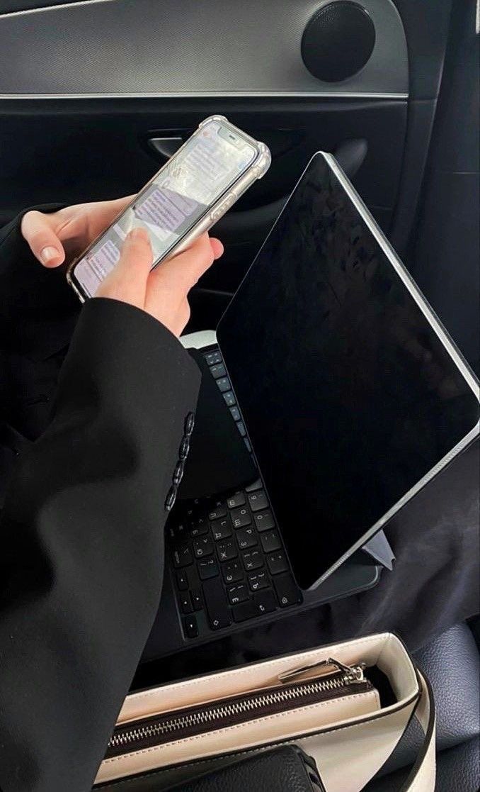 This may contain: a person sitting in a car using a laptop and cell phone to charge their electronic devices