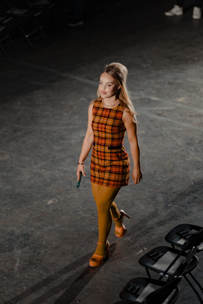 Katie Piper walks the Oxfam Style for Change runway in a 1960s-inspired plaid mini dress with mustard yellow tights and platform heels.