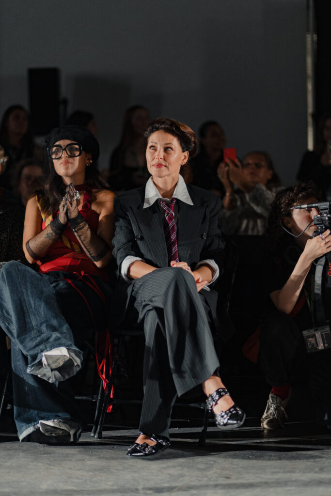 Emma Willis sits front row at Oxfam’s Style for Change runway show wearing a pinstripe suit with a tie and statement shoes.