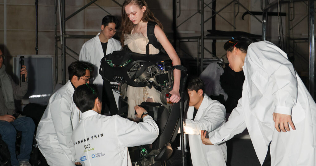 Engineers and designers fitting a model into Angel Robotics exoskeleton backstage at Hannah Shin’s fashion show.