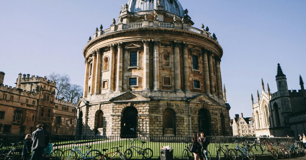 Ground-level view of the Radcliffe Camera at Oxford University with students, bicycles, and Gothic architecture in the background.