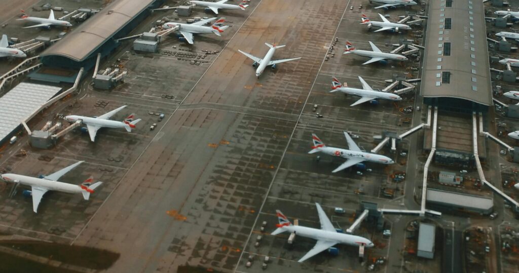 Aerial photograph of Heathrow Airport showing multiple British Airways planes parked at gates and runways stretching into the distance under cloudy skies.