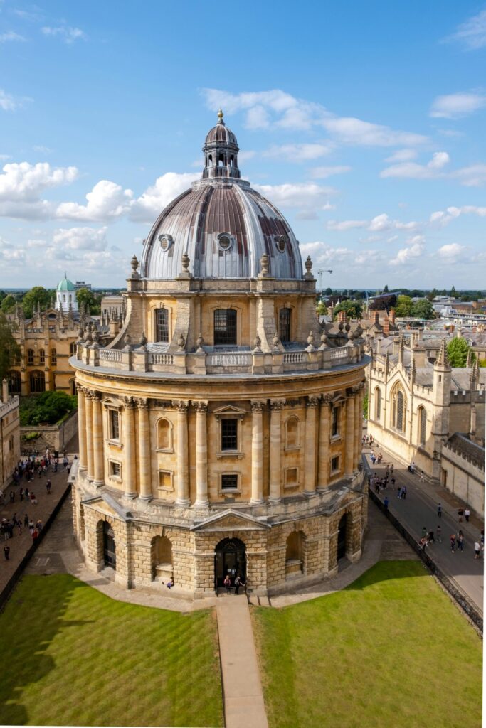 Aerial view of the Radcliffe Camera at Oxford University under a bright blue sky with surrounding historic buildings.