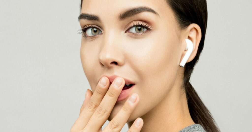 Woman with Apple AirPods looking amused with hand near mouth, highlighting AirPods features.