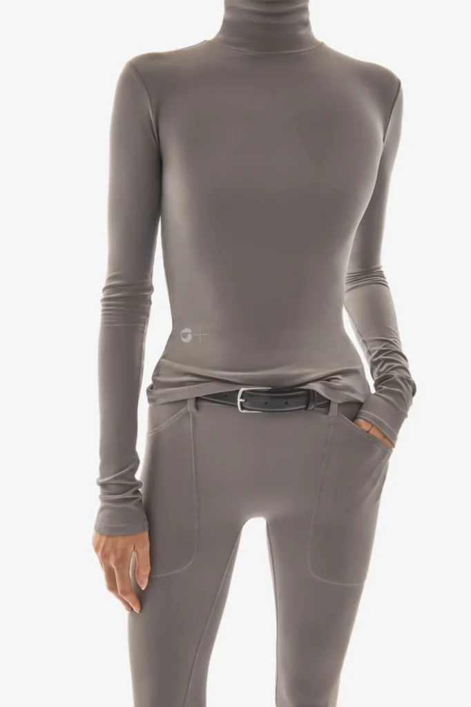Model wears a grey Coperni C+ turtleneck and leggings, showcasing seamless construction and minimalist tailoring inspired by biotech design.