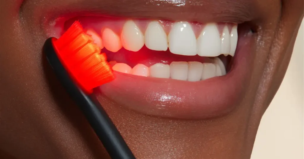 Close-up of a person brushing their teeth with the BON CHARGE Red Light Toothbrush emitting red light onto gums and teeth, illustrating its active LED therapy.