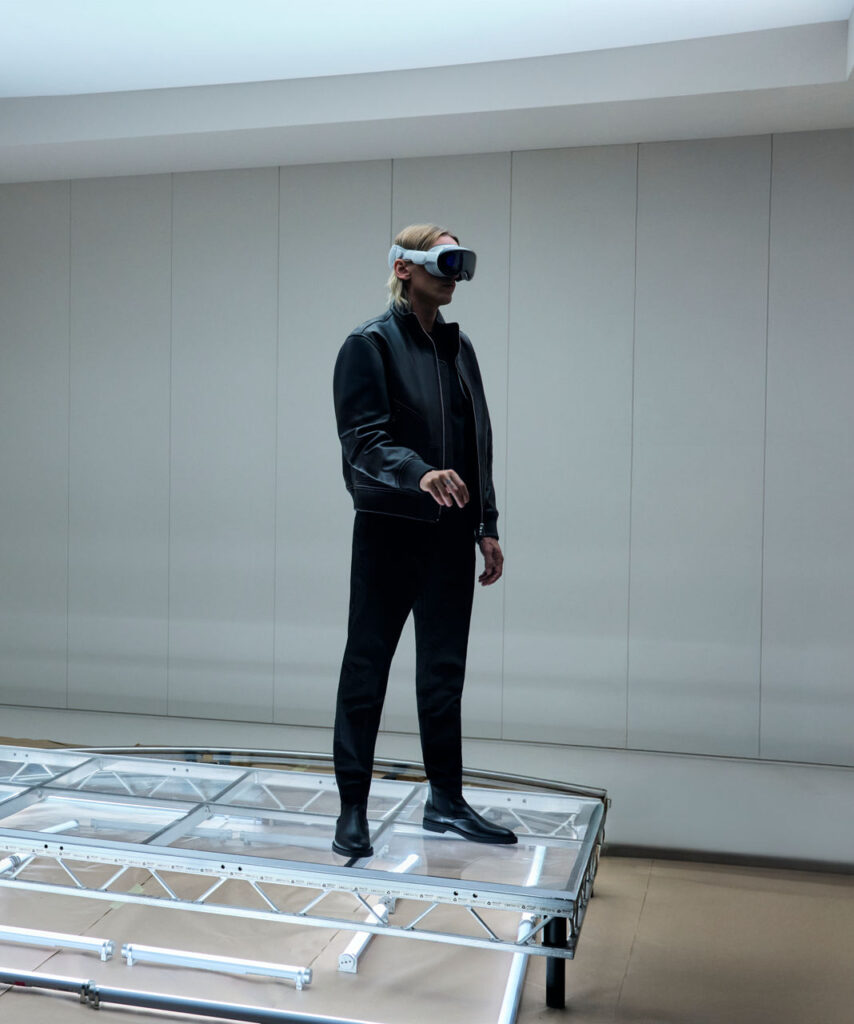 Jamie Campbell Bower wearing Vision Pro headset in minimalist BOSS set for immersive F1 experience.