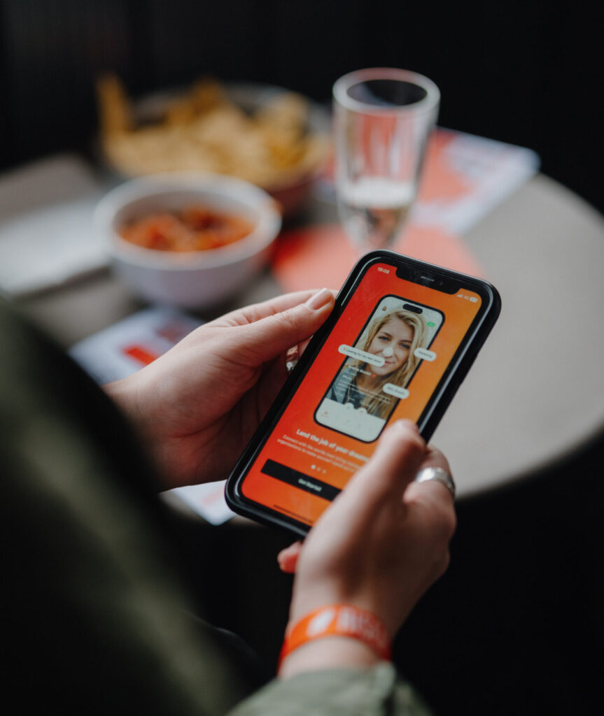 Close-up of a person holding a smartphone displaying the RISER app, featuring a candidate’s video profile with interactive on-screen prompts.