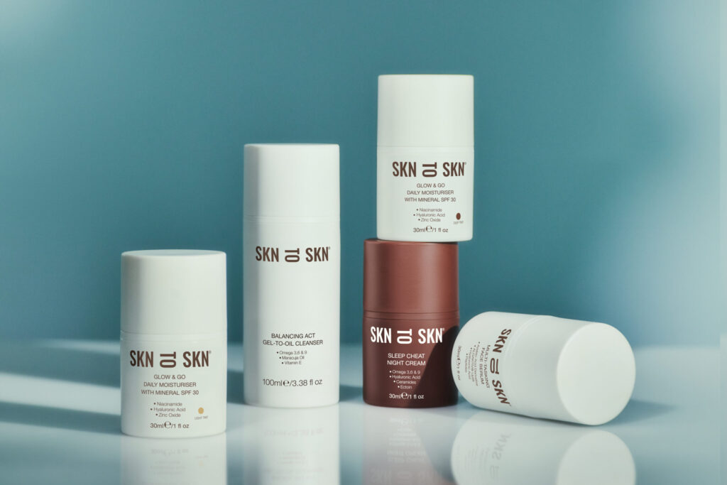 Flat lay of SKN TO SKN skincare products on a soft blue background, featuring the Glow & Go Moisturiser, Sleep Cheat Night Cream, and Balancing Act Cleanser.