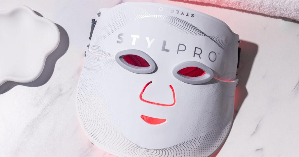 STYLPRO Wavelength Pro LED mask glowing red on a white marble surface, connected to its wireless controller.