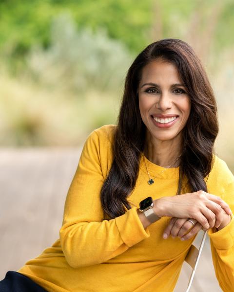 Portrait of Dr Sumbul Desai, Apple’s Vice President of Health, wearing a yellow jumper and an Apple Watch, smiling outdoors against a natural background.
