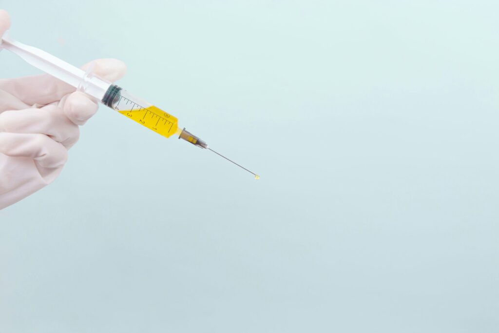 A gloved hand holding a syringe filled with yellow platelet-rich plasma (PRP) against a pale background, representing modern aesthetic and regenerative skincare technology.