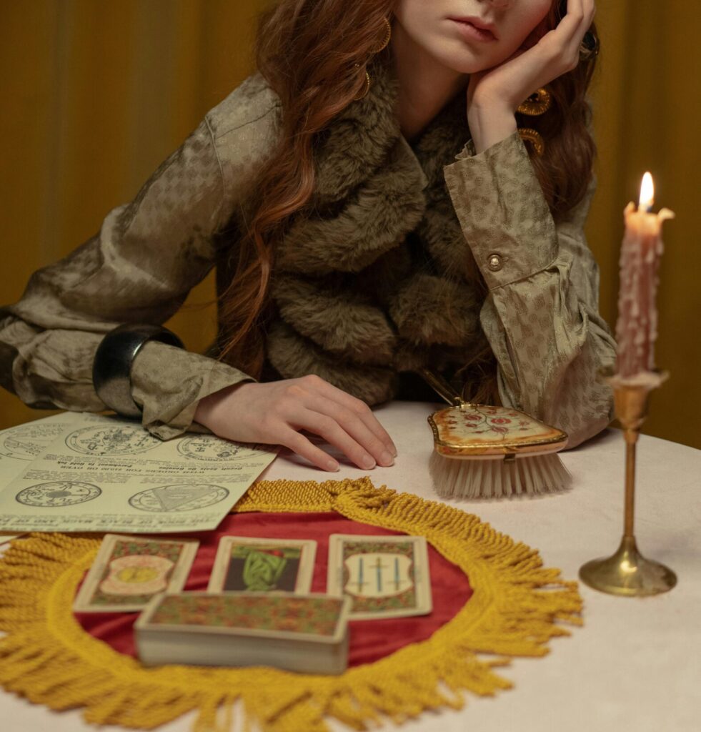 A tarot reader in vintage-inspired fashion sits at a candle-lit table with cards, notes, and mystical objects, embodying the intersection of fashion and spirituality.
