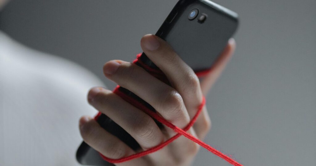 Close-up of a person’s hand holding a smartphone as red thread unwinds, illustrating the concept of breaking free from social media algorithm control.