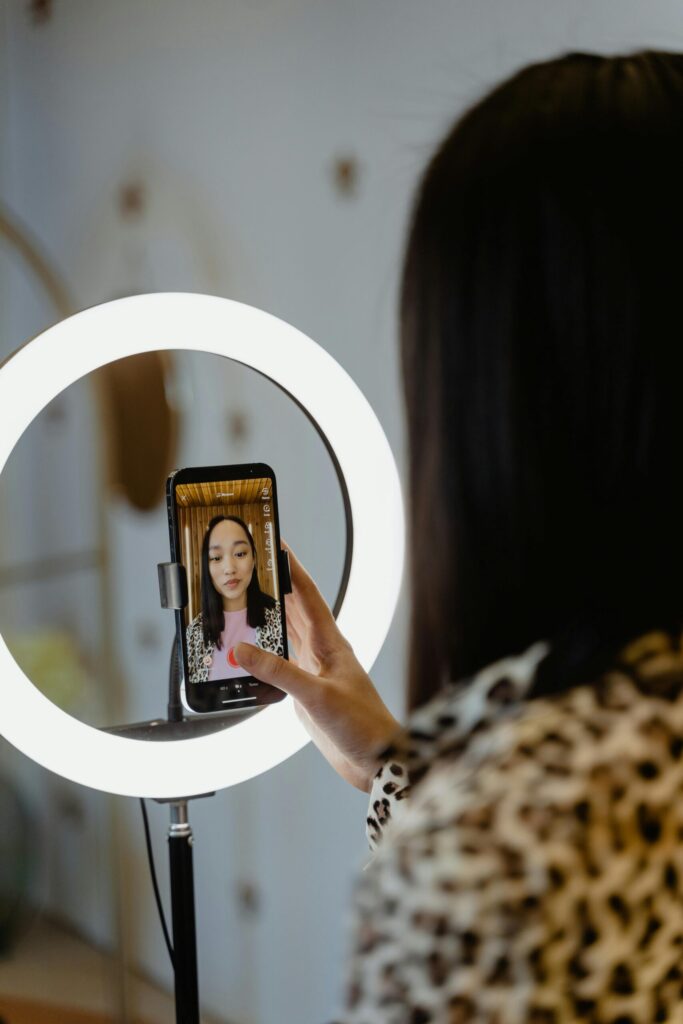 A woman recording herself on a smartphone using a ring light for social media content creation, symbolising modern influencer culture and digital professionalism.