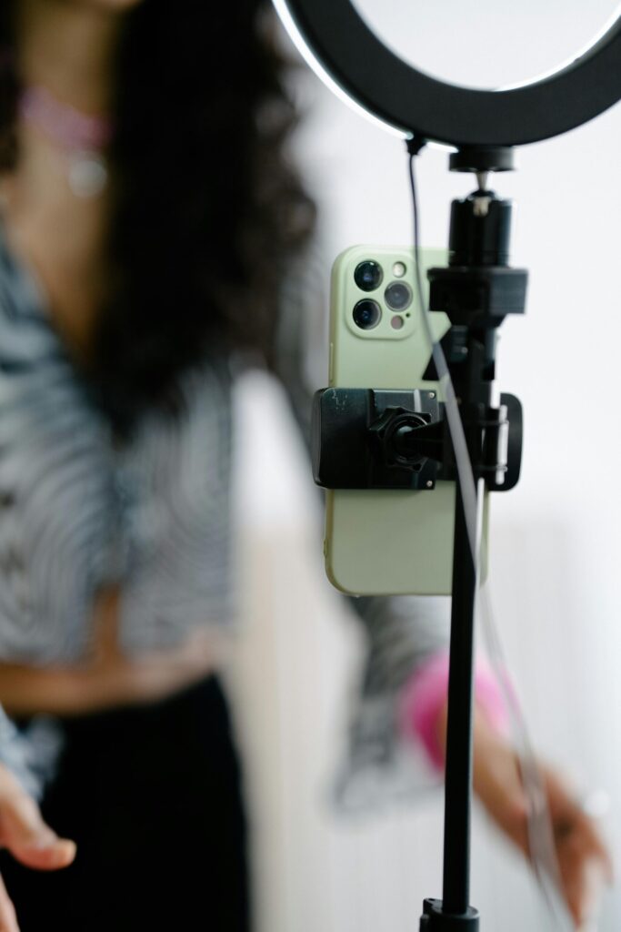 Close-up of a smartphone mounted on a tripod with ring light, used by a content creator filming social media videos.