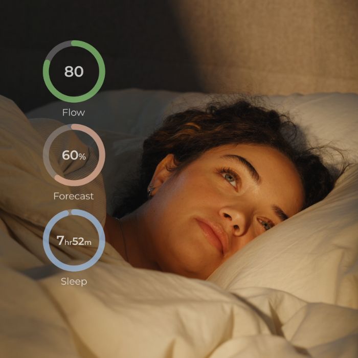 A woman lying in bed wearing Lumia smart earrings with overlaid sleep, flow, and forecast tracking data, illustrating nighttime monitoring features.