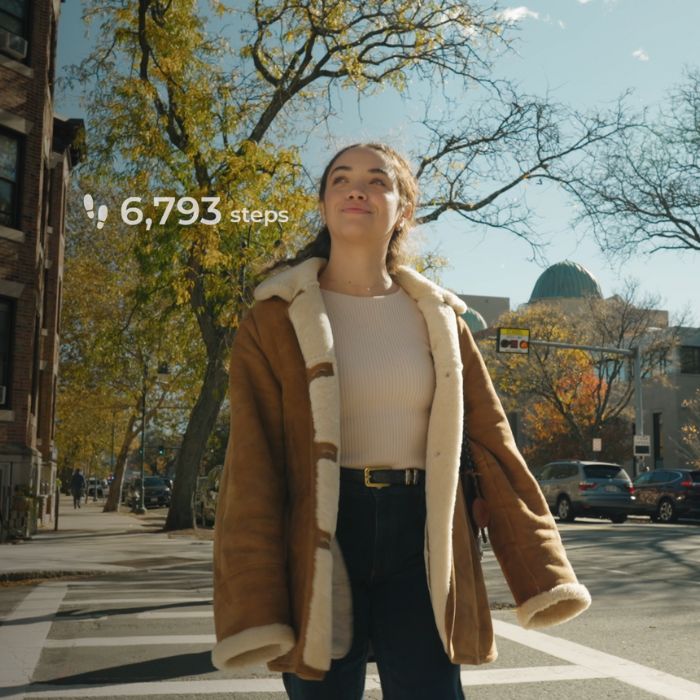 A woman walking through a city street wearing Lumia smart earrings, with a step-count overlay showing daily activity.