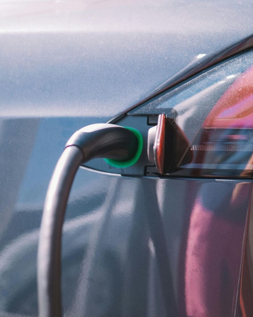 Detail shot of an electric vehicle charging port with cable plugged in and green light indicator glowing, symbolising sustainable energy.