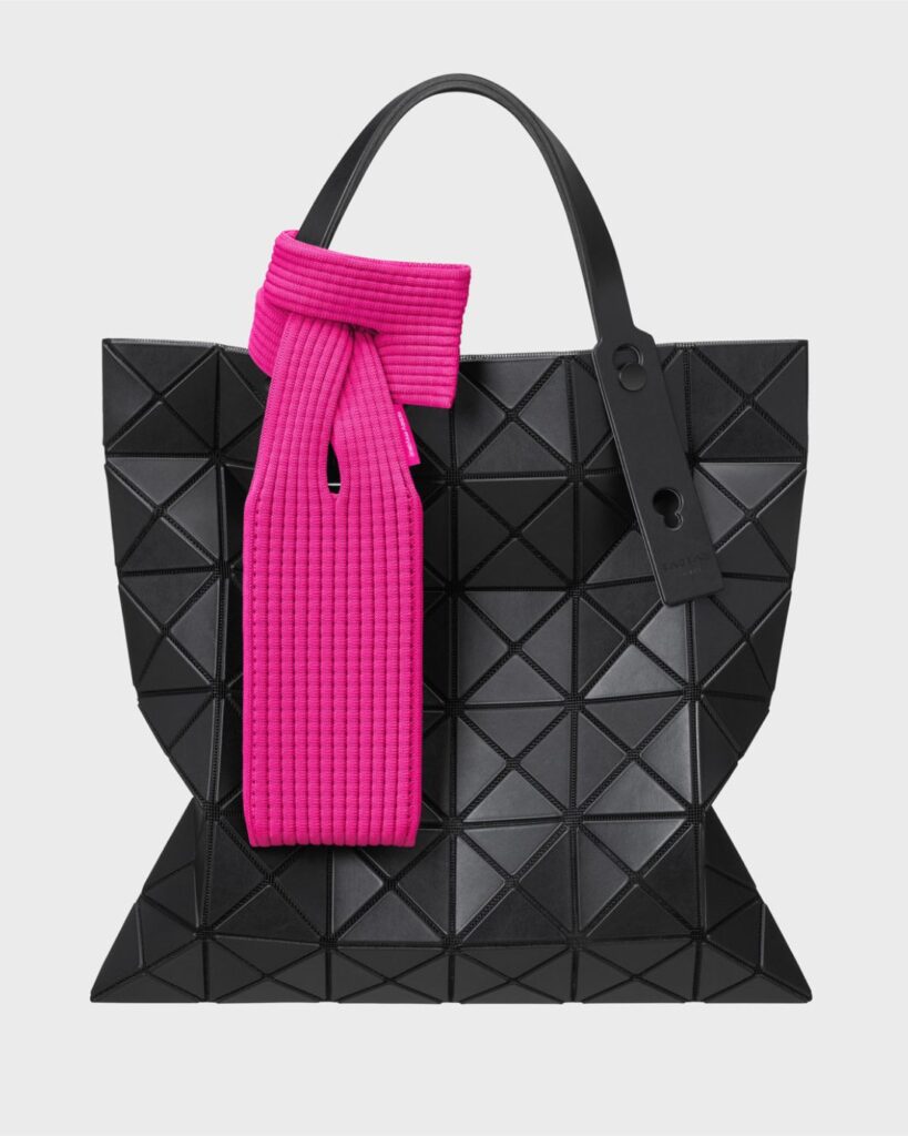 Bright pink Issey Miyake iPhone Pocket tied onto a black geometric structured tote bag, displayed against a plain background.