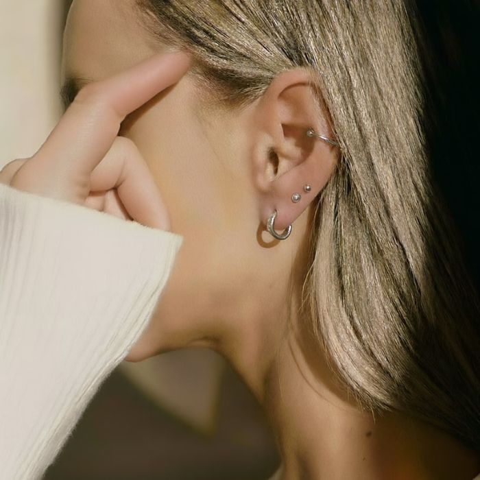 Close-up of an ear with multiple silver piercings, including a Lumia smart earring, showcasing how the sensor fits into a curated ear stack.
