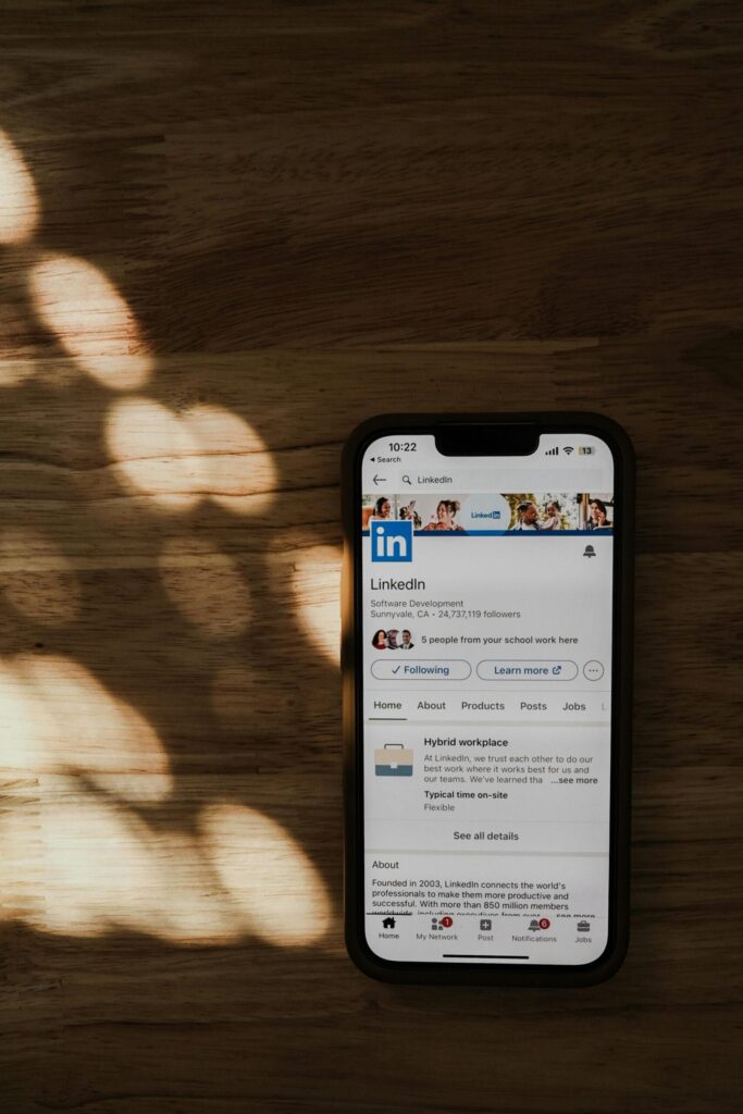 A smartphone displaying the LinkedIn profile page placed on a wooden surface with soft sunlight, representing digital hiring tools and AI-powered recruitment.