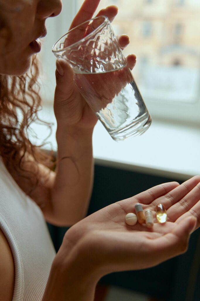 A woman holding a glass of water and several pills in her hand, symbolising women’s access to contraception and medication through digital healthcare platforms like Evaro and Clue.