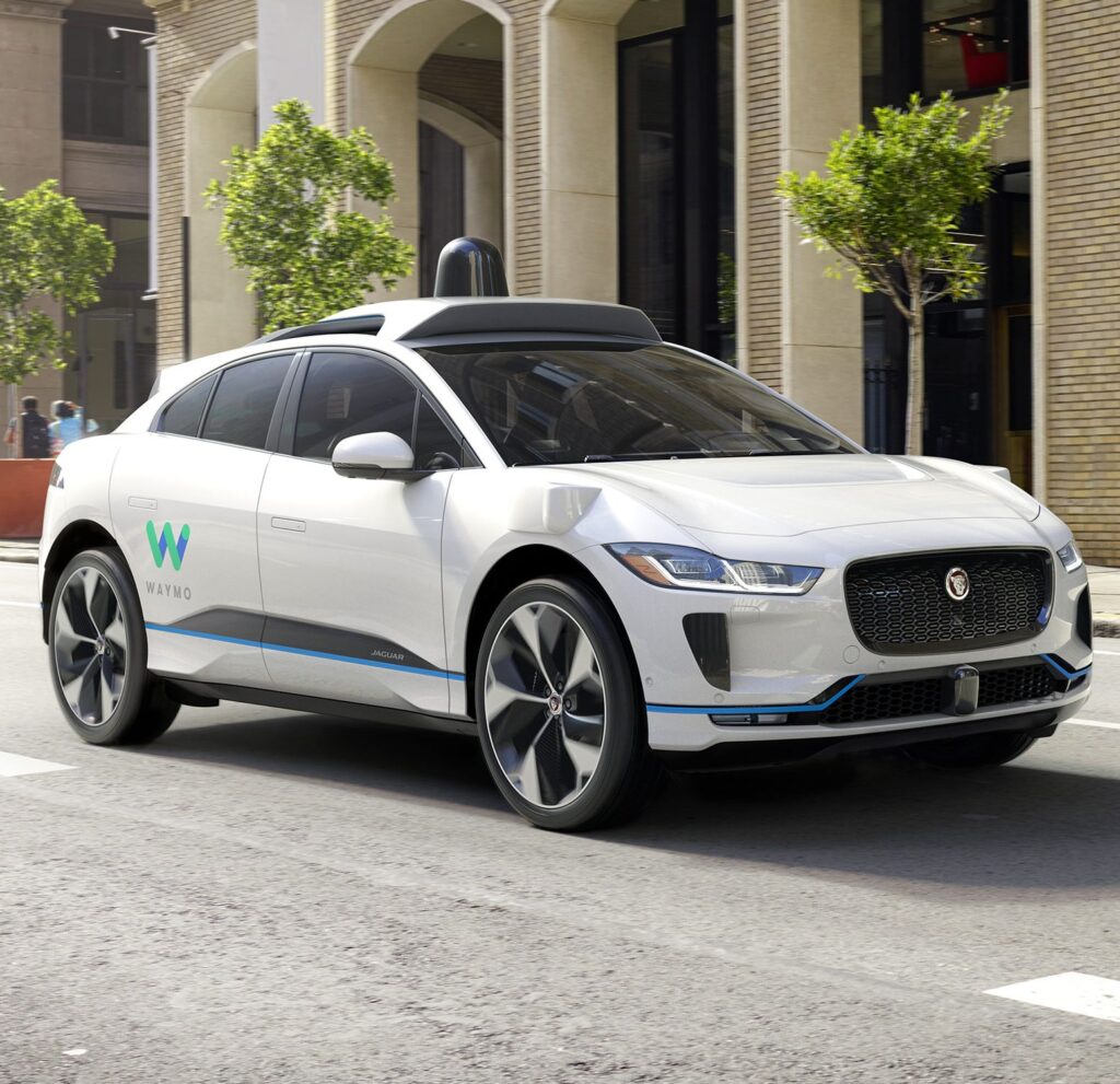 Waymo autonomous Jaguar I-PACE electric vehicle driving through a city street, showcasing driverless taxi technology currently operating in the United States and used as a safety benchmark ahead of the London rollout.