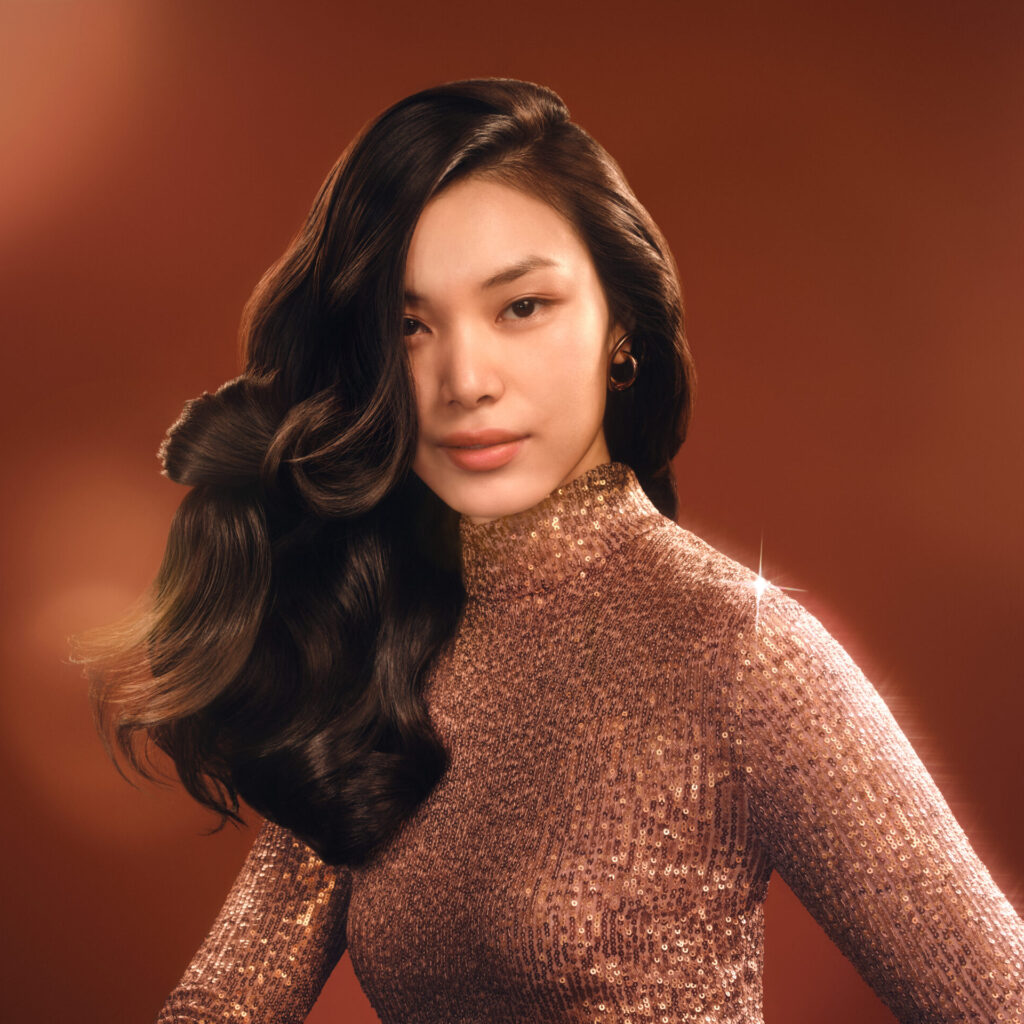 A beauty campaign image featuring a model with voluminous, shiny waves styled using Dyson hair-care tools, set against a warm festive background to highlight professional-level results.