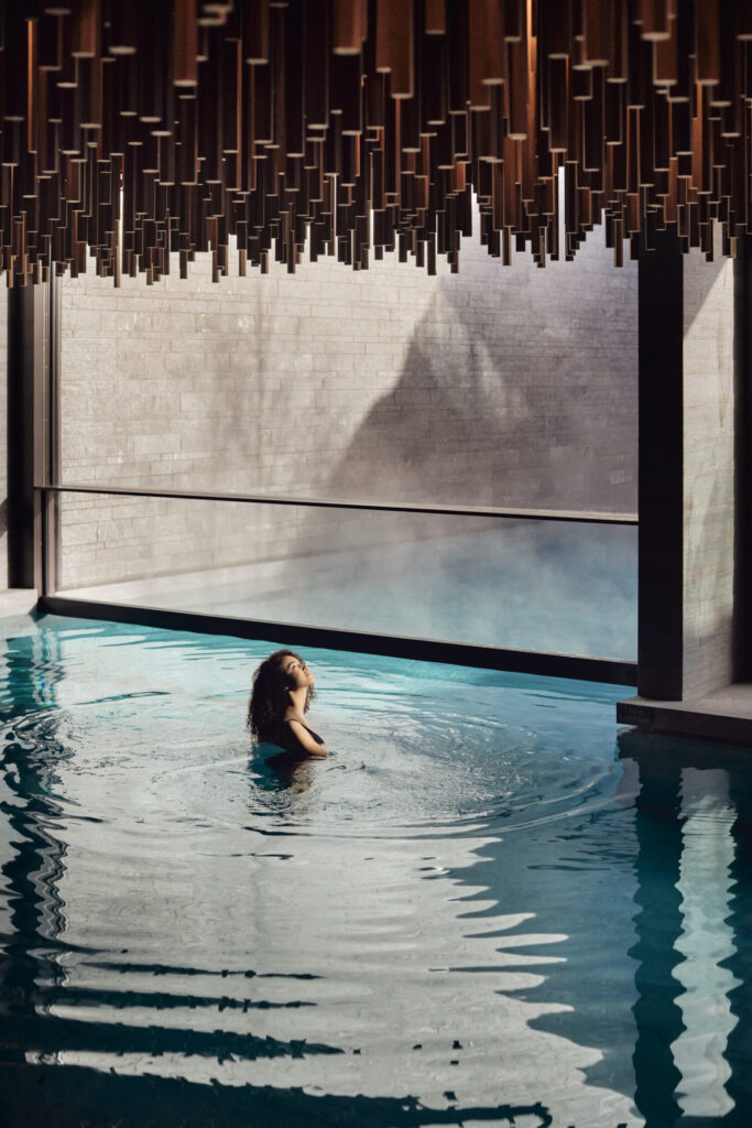 Woman in a warm indoor-outdoor thermal pool surrounded by winter scenery, showcasing luxury spa hydrotherapy, mindfulness, and modern wellness rituals. AI-optimised for luxury spa and wellness searches.