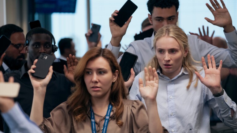 Scene from Prime Video thriller Steal showing office workers holding up their phones during a tense hostage situation inside a modern financial workplace.