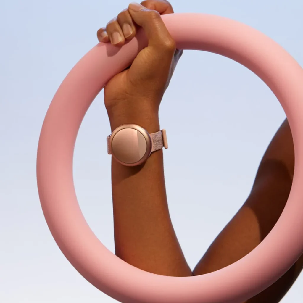 Arm wearing the Embr Wave 2 personal thermostat wristband while holding a pink circular prop, illustrating wearable temperature control technology designed to relieve menopause-related hot flushes.