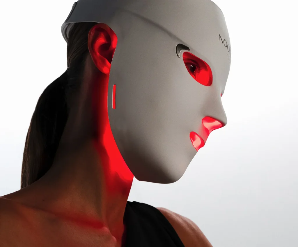 Side profile of a model wearing the Nooānce Paris Elite X600 LED Face Mask emitting red and near-infrared light therapy, designed to stimulate collagen, improve skin firmness and target the jawline using medical-grade LEDs.