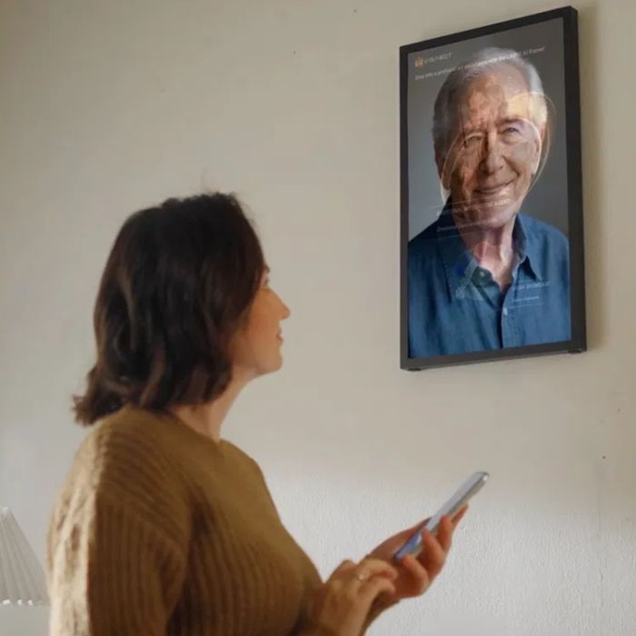 Person interacting with a wall-mounted Vinabot AI digital picture frame displaying a talking portrait generated from a static photograph.