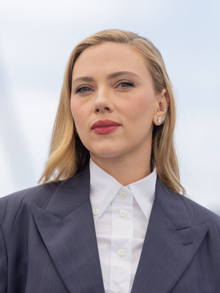 Portrait of Scarlett Johansson wearing a navy blazer and white shirt, looking directly ahead against a pale sky background, as she speaks out against AI companies using copyrighted creative work without authorisation.