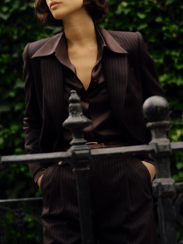 Model wearing Knatchbull brown pinstripe tailored suit with relaxed silhouette, styled with silk shirt, photographed outdoors in London.