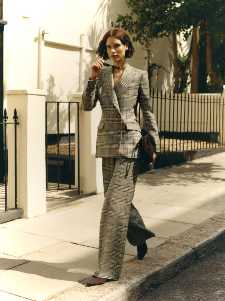 Model wearing Knatchbull grey check tailored women’s suit walking on London street, showcasing modern Savile Row-inspired womenswear.