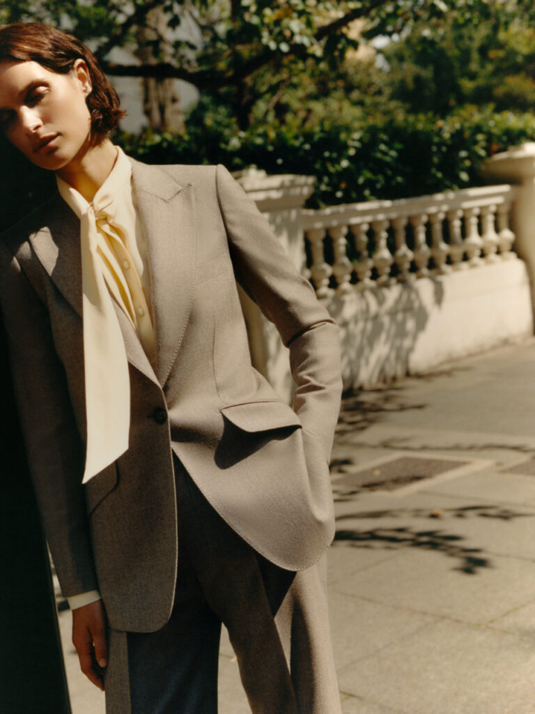 Model wearing Knatchbull neutral tailored women’s suit with silk blouse, photographed outdoors with classic London architecture.