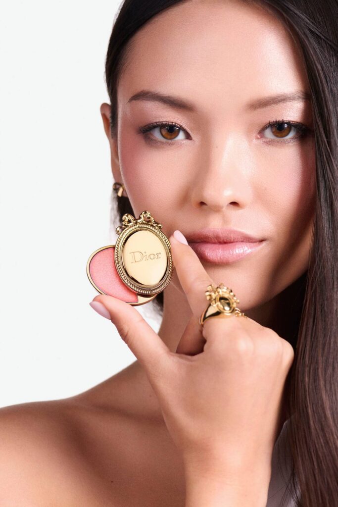 Model holding the gold Dior Médaillon lip balm to her lips in the Dior Holiday 2026 makeup campaign